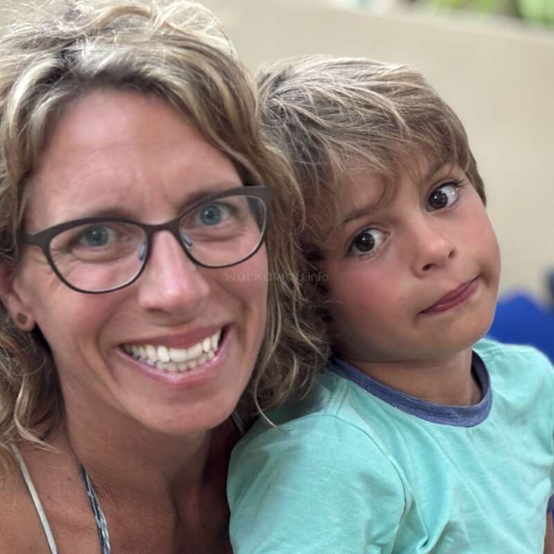 A woman with glasses and a big smile poses closely with a young boy who has a neutral expression, light hair, and a mint green shirt.
