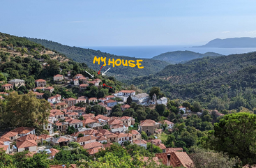 Un pintoresco pueblo con casas de tejados rojos enclavado entre exuberantes colinas verdes, con vistas al mar lejano. "Mi casa" está resaltada con una alegre anotación amarilla.