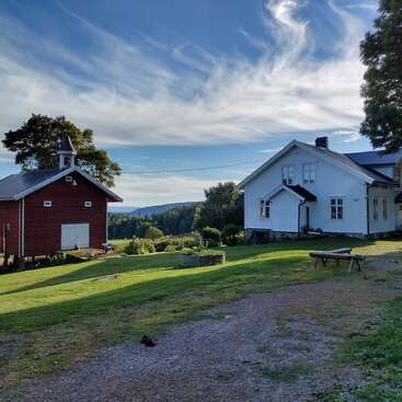 The image depicts a serene rural scene featuring two houses, a red barn, and a lush green lawn, set against a picturesque blue sky with white clouds.