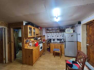 Esta acogedora cocina cuenta con armarios de madera, un frigorífico, un microondas, estantes abiertos con vajilla, una cortina estampada, una luminosa lámpara de techo y un ambiente rústico con una decoración práctica.