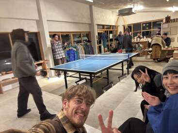A group of friends are enjoying an indoor gathering with a ping pong table, smiles, casual clothing, and peace signs, creating a lively, relaxed atmosphere.