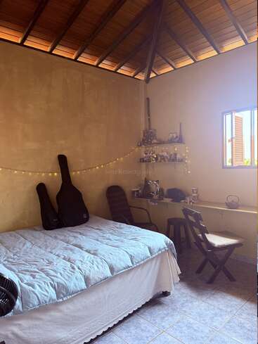 Esta acogedora habitación cuenta con un techo inclinado de madera, una cama bien hecha, guitarras, luces de cuerda, un pequeño escritorio con estanterías, una silla y luz natural.