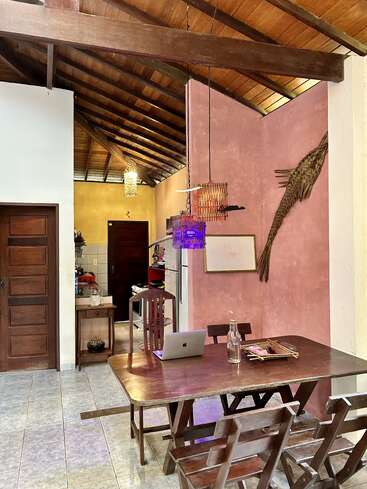 Este acogedor comedor cuenta con muebles de madera, techo inclinado de madera, pared de acento rosa, luces colgantes, ordenador portátil, botella de cristal, decoración tejida y un ambiente cálido y acogedor.