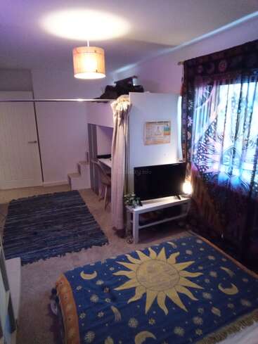 Une chambre douillette avec un couvre-lit à thème céleste, un lit superposé, un tapis bleu, une tapisserie murale, une télévision, un éclairage doux et un rideau à motifs près de la fenêtre.