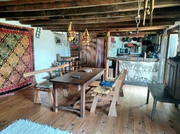 Cette salle à manger rustique et chaleureuse se compose de meubles en bois, de lampes suspendues colorées, d'une tapisserie murale vibrante, de poutres apparentes, d'un bar à motifs et d'une atmosphère accueillante et chaleureuse.