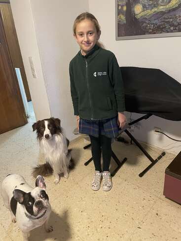 A smiling girl stands indoors next to a brown and white dog and a black and white dog. Behind her is a keyboard and a Van Gogh painting.