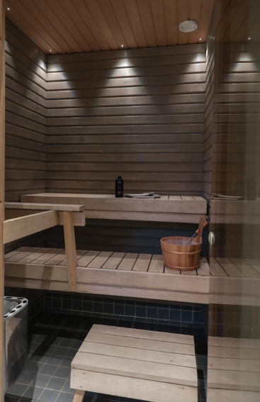 Cette image montre un sauna moderne en bois avec des bancs, un seau et une louche, une bouteille d'eau et un éclairage encastré. Le sol est carrelé, ce qui crée une atmosphère agréable.