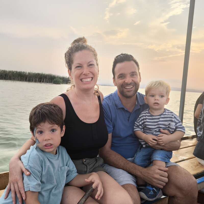 A smiling family of four sits together on a wooden bench by the water at sunset, enjoying a peaceful and joyful boat ride outdoors.