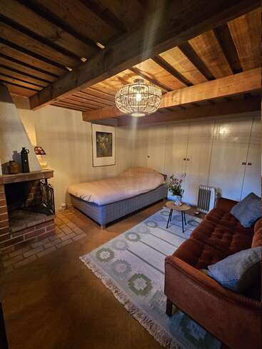 Ein gemütliches Zimmer im Landhausstil verfügt über eine Holzdecke, einen gemauerten Kamin, ein weiches Bett, einen gemusterten Teppich, ein bequemes Sofa, stimmungsvolle Beleuchtung und eine minimalistische Einrichtung.