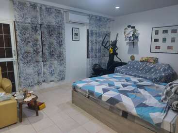 A cozy bedroom with patterned curtains, a double bed, a small couch, exercise equipment, artwork on white walls, a small table, and an air conditioner.