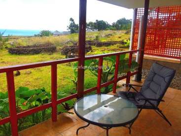 The image depicts a serene outdoor setting, featuring a patio with a table and chair, overlooking a grassy area and the ocean in the distance.