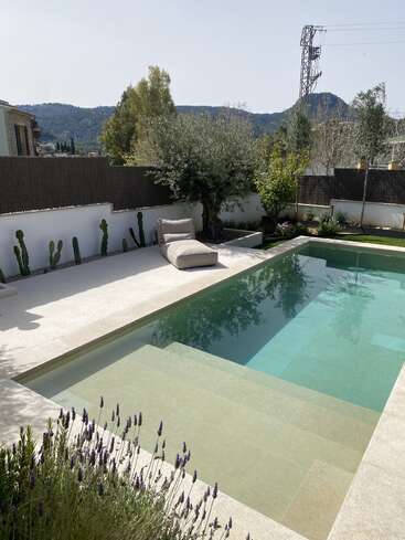 Ein ruhiger Garten mit einem modernen Pool, bequemen Liegestühlen, Lavendelpflanzen, Kakteen entlang der Mauer und einem malerischen Bergblick im Hintergrund.