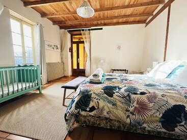 Dieses gemütliche Schlafzimmer besticht durch eine farbenfrohe Tagesdecke, eine rustikale Holzdecke, ein großes Fenster mit leichten Vorhängen, ein grünes Kinderbett, eine Bank und natürliches Tageslicht. Eine einladende Atmosphäre.