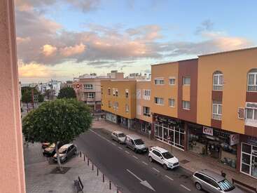 Une scène de rue urbaine calme au coucher du soleil avec des bâtiments jaunes, des voitures garées, des arbres verts, un magasin de tatouage et un ciel magnifique avec des nuages colorés au-dessus de la tête.