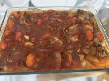 Un plat de cuisson en verre rempli d'un ragoût copieux de légumes, notamment de carottes et d'oignons, dans une sauce riche de couleur rouge-brun, prêt à être servi.