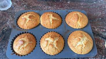 Cette image montre six muffins dorés fraîchement cuits dans un moule à muffins en silicone sur un comptoir marbré, chacun présentant des fissures intéressantes sur le dessus.