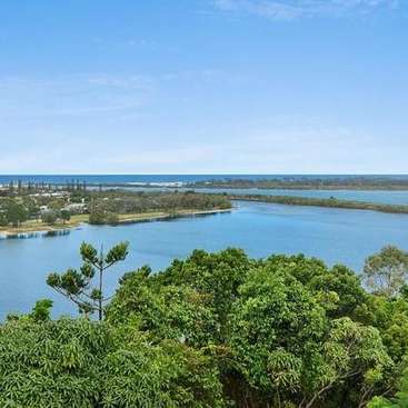 La imagen representa un paisaje sereno con una masa de agua, vegetación exuberante y un cielo azul, con una línea de horizonte lejana.