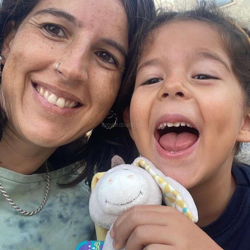 A woman and a child are smiling joyfully at the camera. The child is holding a soft toy, creating a warm, happy, and playful atmosphere together.