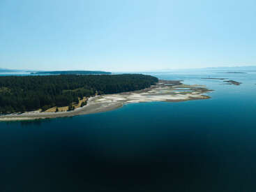Eine ruhige Luftaufnahme einer Küstenlandschaft mit üppigen grünen Wäldern, sandigen Ufern, ruhigem blauen Wasser und einem klaren Himmel an einem sonnigen, friedlichen Tag.