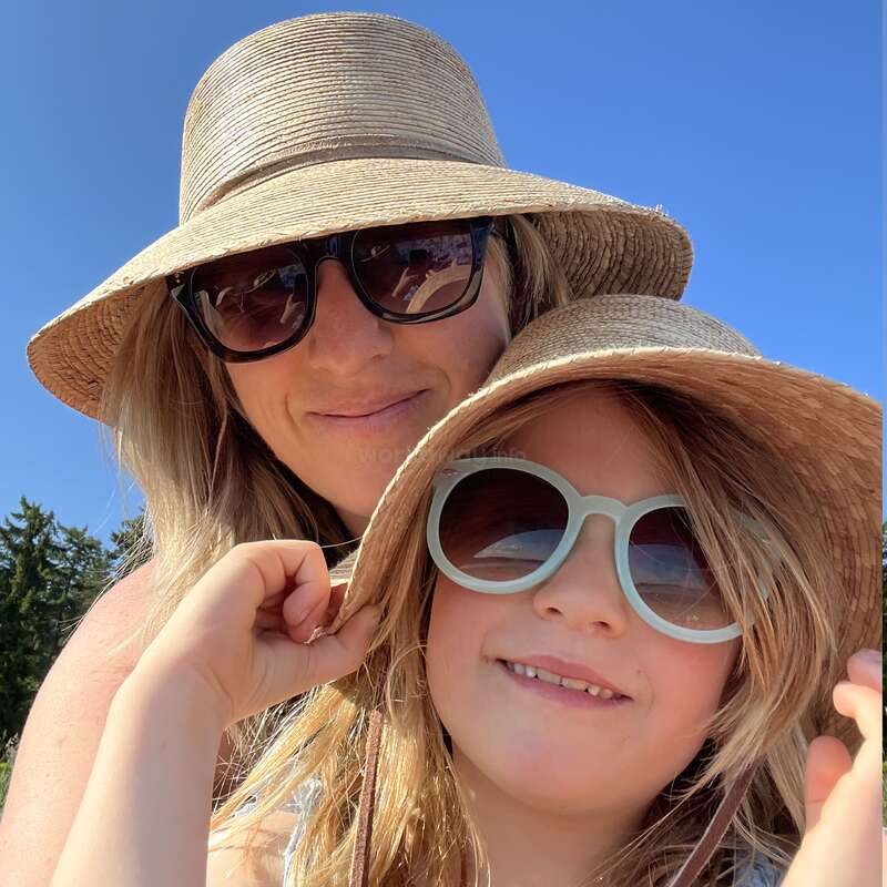 L'image montre une femme et un enfant portant des chapeaux de paille et des lunettes de soleil, posant ensemble devant un ciel bleu avec des arbres en arrière-plan.