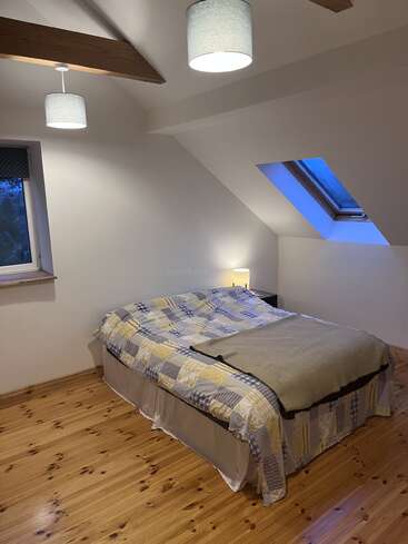 Dieses gemütliche Schlafzimmer im Dachgeschoss hat ein Doppelbett mit einer Patchworkdecke, Holzböden, eine Nachttischlampe, schräge Decken, freiliegende Balken und Dachfenster.