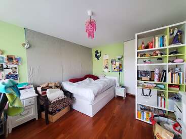This cozy bedroom features a comfortable bed, colorful decor, bookshelves filled with books, personal items, a small desk, wooden floor, and pastel green walls.