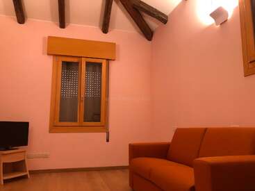 The image depicts a cozy living room with a salmon-colored couch, wooden beams on the ceiling, a window with a brown valance, and a TV on a small wooden table.