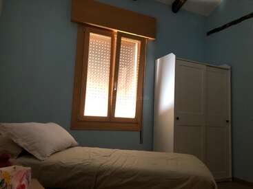 The image depicts a small bedroom with a bed, window, and closet, featuring light blue walls and a white ceiling, with natural light entering through the window.