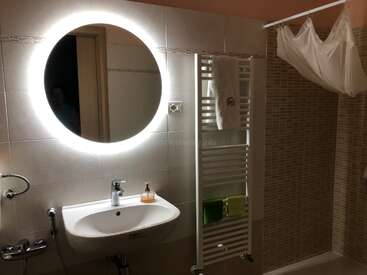 The image depicts a bathroom with a round mirror, white sink, and towel rack, featuring a white shower curtain and tiled walls in a neutral color scheme.