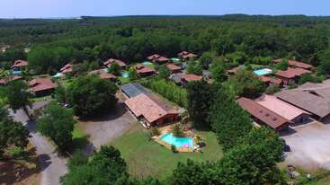 This aerial image shows a peaceful resort with several wooden cabins surrounded by lush green trees, swimming pools, and open spaces, set in a dense forest landscape.