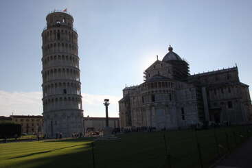 L'image montre la tour penchée de Pise et la cathédrale de Pise en Italie, dans un ciel clair, avec des personnes admirant les célèbres monuments architecturaux.