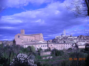 Cette image montre une ville italienne pittoresque à flanc de colline avec des bâtiments historiques, une église proéminente, une végétation luxuriante et des nuages d'un bleu spectaculaire sous un ciel éclatant. Avril 2010.