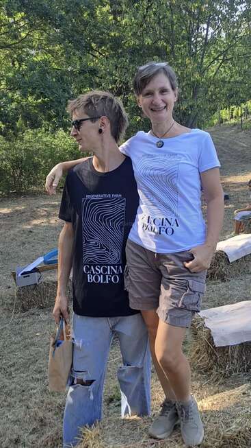 The image shows two people standing together in a grassy area, with trees in the background, wearing matching t-shirts with a logo that says \"Regenerative Farm Cascina Bolfo\".