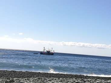 The image depicts a serene ocean scene with a small boat floating on the water, set against a backdrop of a blue sky with white clouds and a rocky shoreline.