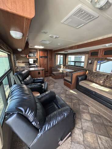 L'intérieur de ce véhicule récréatif confortable comprend des fauteuils inclinables en cuir noir, un coin repas, une kitchenette, de grandes fenêtres, des armoires en bois et de nombreuses places assises, créant ainsi un espace de vie confortable et pratique pour les voyages.