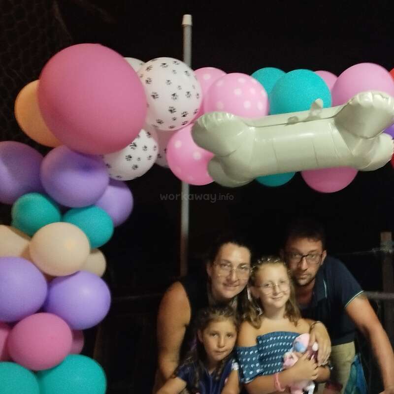 Une famille de quatre personnes pose joyeusement sous une arche de ballons colorés, y compris un ballon en forme d'os, lors de ce qui semble être un événement festif ou une célébration.