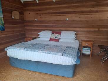 Este acogedor dormitorio cuenta con una cama doble con ropa de cama blanca y azul, paredes de madera, dos mesillas de noche, un cojín decorativo y una decoración minimalista, que crea un ambiente rústico.