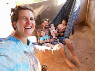 A happy family enjoys time together. One person takes a selfie, smiling brightly, while the others relax in a hammock, laughing, barefoot, and surrounded by warmth.