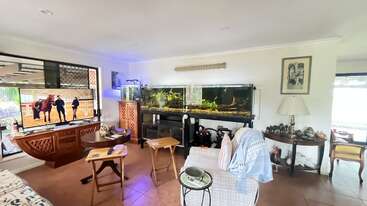 A cozy living room featuring a large TV, two aquariums, wooden furniture, side tables, a comfortable chair with blankets, decorative lamps, and various decor items.