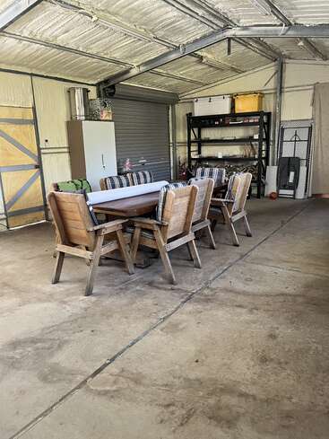 This image shows a spacious garage with a wooden table and six cushioned chairs, metal shelves, a cabinet, insulated walls, and various storage containers and items.