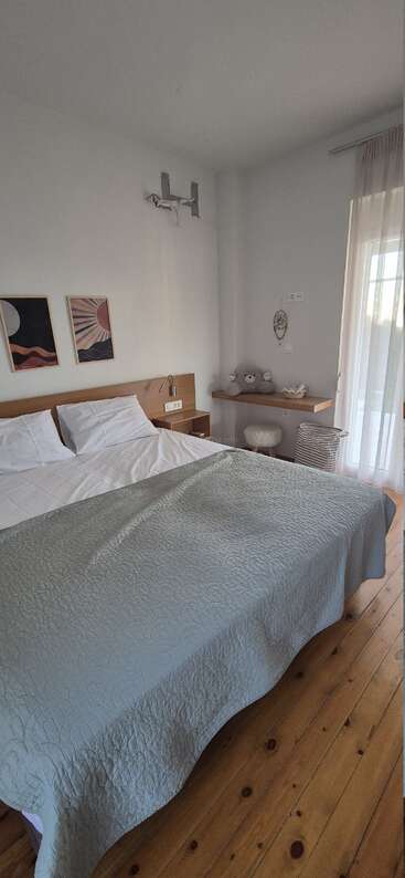 Chambre moderne avec parquet, lit bien fait, tableau abstrait au mur, un coin douillet avec un ours en peluche, un bureau, un tabouret moelleux et des rideaux vaporeux laissant passer la lumière naturelle.
