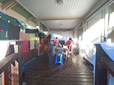 The image depicts a covered wooden deck with a table and chairs, featuring a clothesline with hanging laundry on the left side.