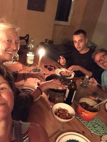 Four people are enjoying a cozy candlelit dinner together. They are smiling, with plates of food, wine, and conversation, creating a warm and inviting atmosphere.