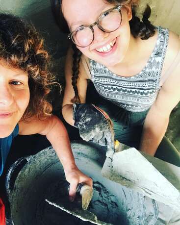 Two smiling people pose for a selfie while working with cement. One holds a trowel, both appear happy and engaged in a creative, hands-on project together.