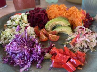 Dieser Teller enthält eine bunte Mischung aus frischem Gemüse: geraspelte Karotten, Rote Bete, Kohl, Zucchini, rote Paprika, Avocadoscheiben, Kirschtomaten und Zwiebeln. Gesund und bunt!