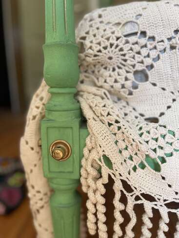 Primer plano de un poste de silla de madera verde, con un perno de latón antiguo y cubierto con una intrincada tela de encaje de ganchillo de color crema.