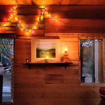 The image depicts a cozy wooden room with a shelf, string lights, and a window, exuding a warm and inviting atmosphere.