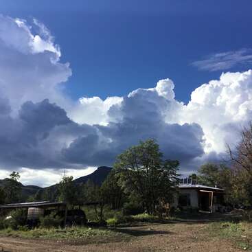 The image depicts a serene rural landscape featuring a house, trees, and a dirt road, set against a backdrop of a blue sky with white clouds.