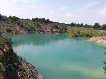 L'image représente un lac serein d'une couleur turquoise éclatante, niché dans un paysage rocheux et entouré d'une verdure luxuriante sous un ciel bleu clair.