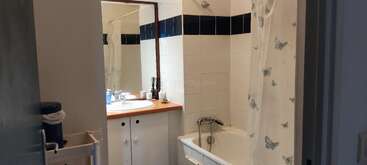 Dieses kleine Bad hat eine weiße Badewanne mit einem Duschvorhang mit Schmetterlingsmuster, einen Waschtisch aus Holz, einen großen Spiegel, Toilettenartikel und weiße Fliesen mit blauen Akzenten.